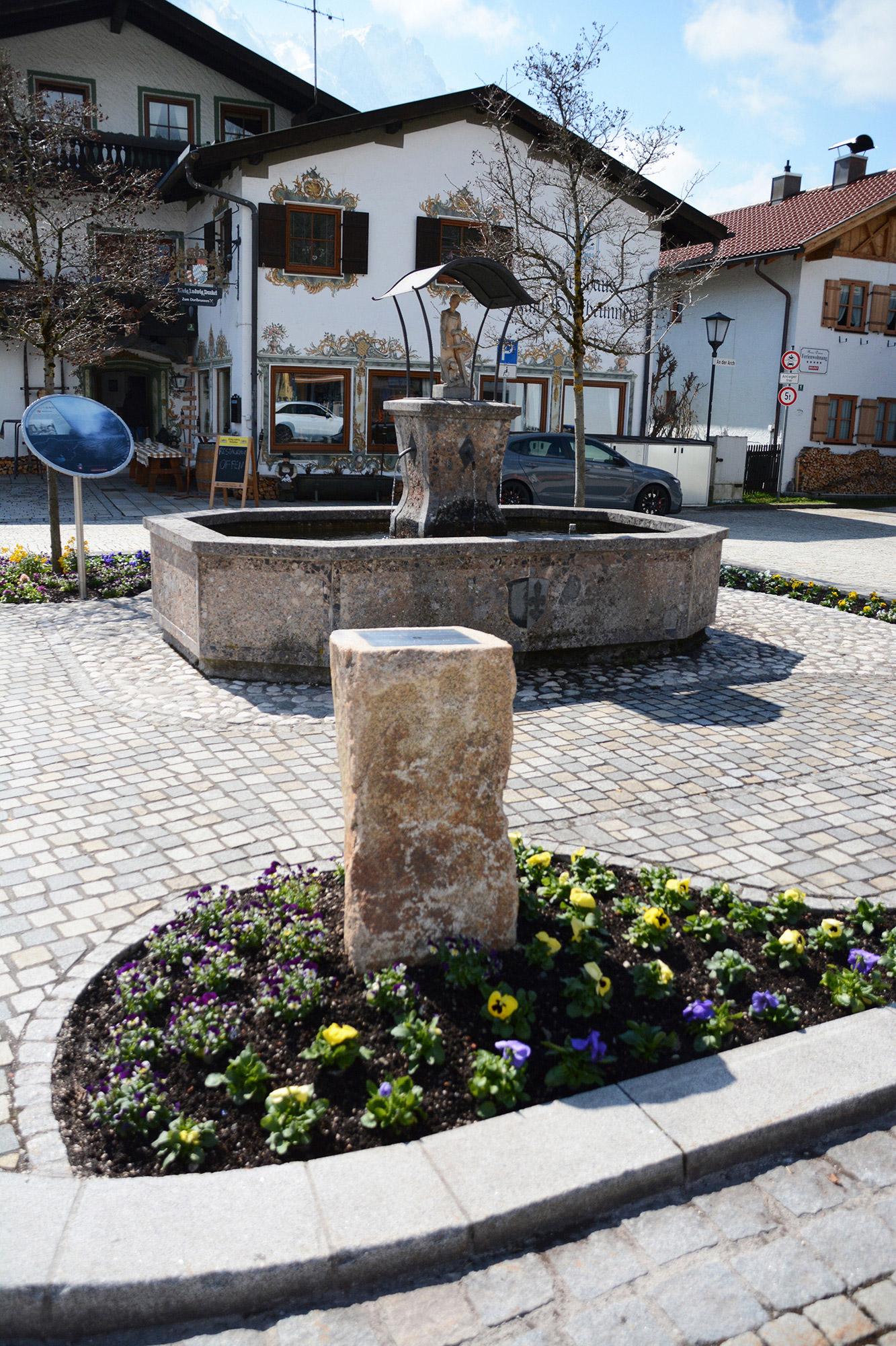 Auf dem Dorfplatz in Grainau sieht man den Geodätischen Referenzpunkt und im Hintergrund einen Brunnen