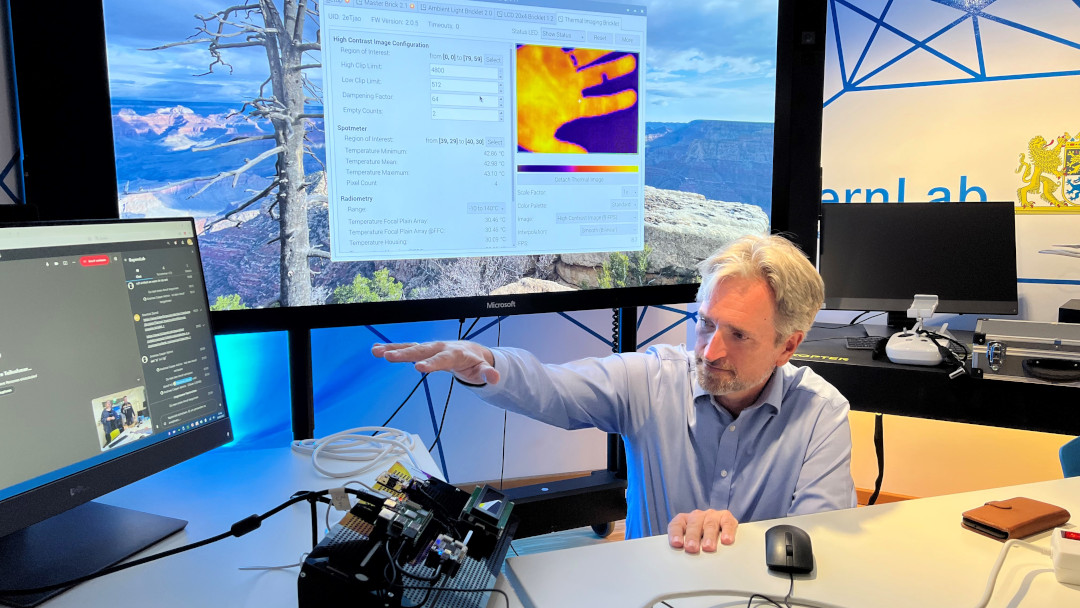 Ein Stammtischteilnehmer hält seine Hand über den Sensor einer Wärmebildkamera. Die Temperatur wird grafisch erfasst, sodass auf einem Bildschirm die Hand in unterschiedlichen Farben zu sehen ist.